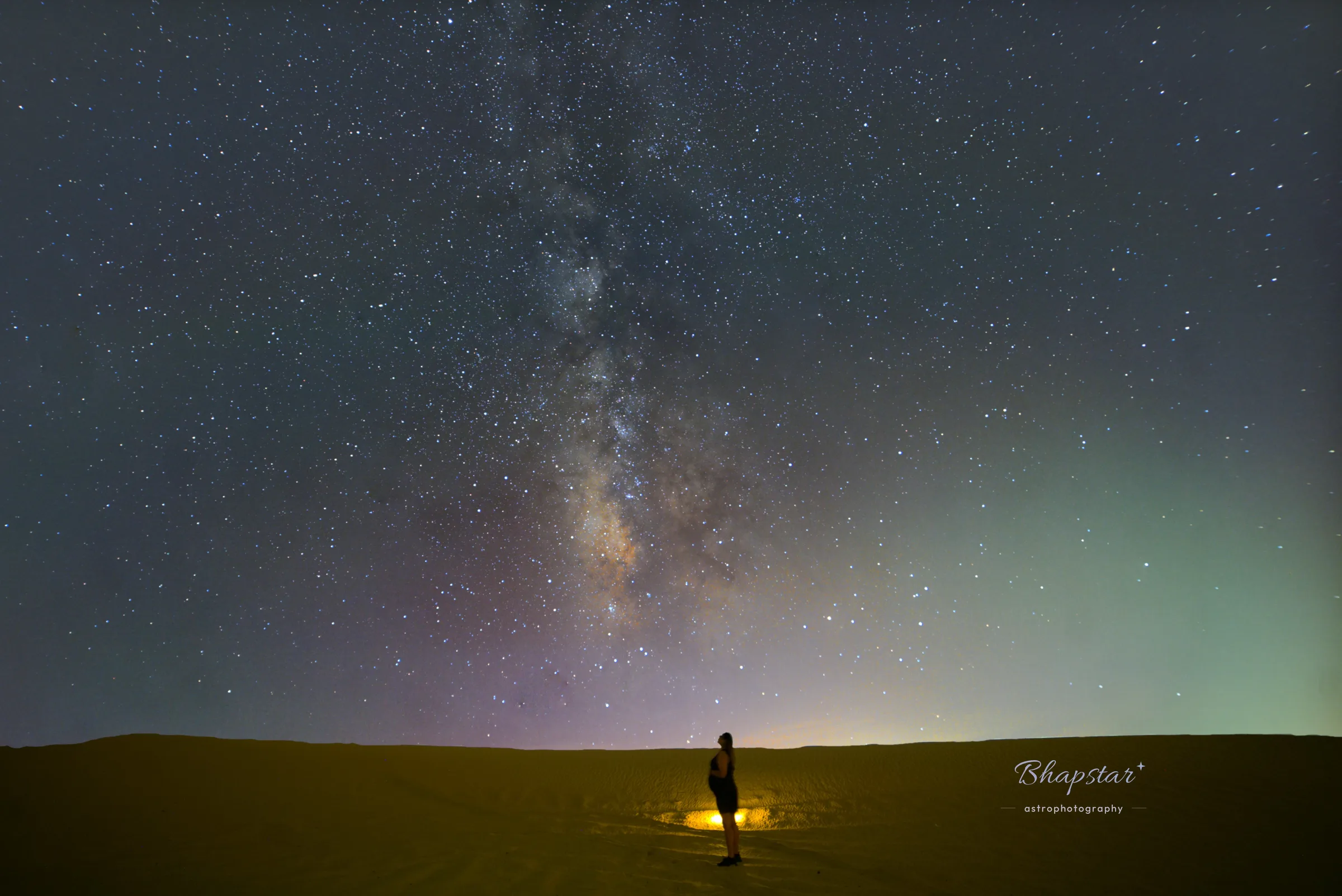 Pregnant woman in silhouette looking up at the Milky Way core above desert sand at night