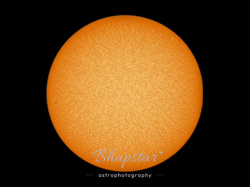 The Sun photographed through a solar filter, an orange disc with small dark sunspots and a darker edge